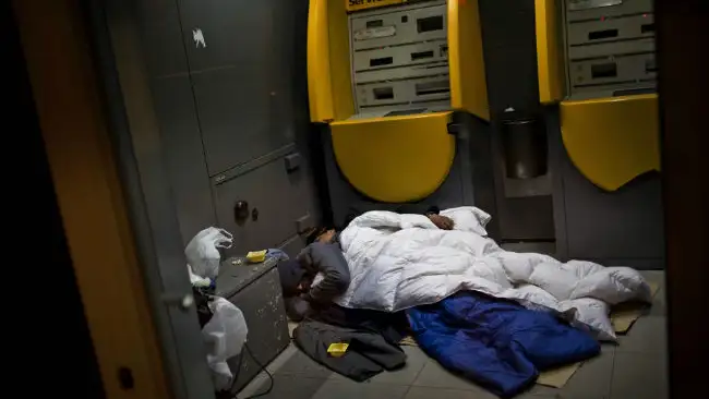 Dos vagabundos duermen en un cajero en Barcelona.