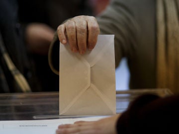 Una persona introduce un sobre en una urna electoral.