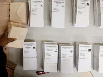 Una persona coloca en la mesa de un colegio electoral las papeletas con las diferentes opciones pol&iacute;ticas