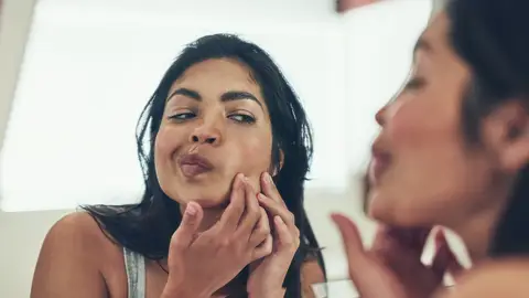 Chica explotándose granos en el espejo. Chica explotándose granos en el espejo.