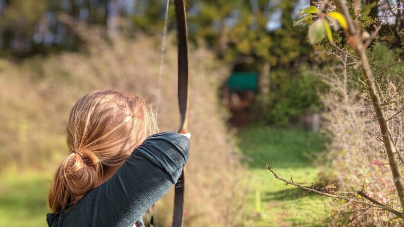 Una madre con su bebé a la espalda caza un jabalí con arco