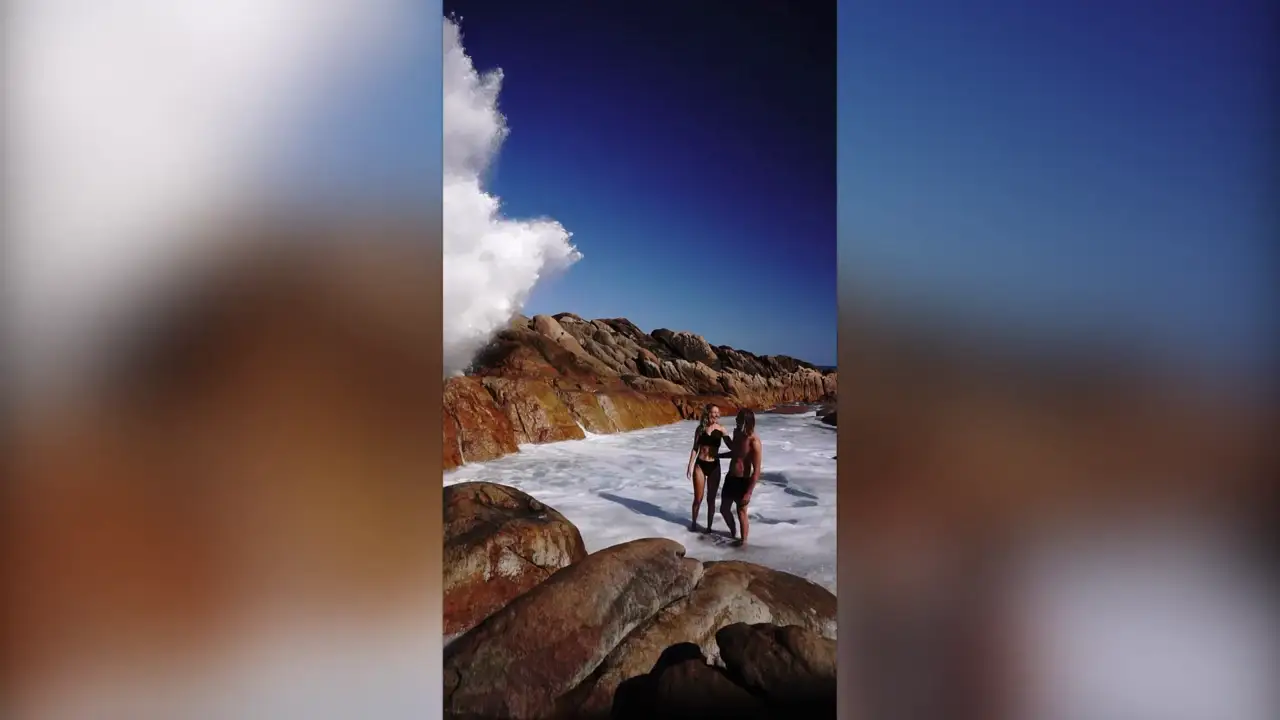 Una pareja estaba posando para una foto en una playa cuando llegó una ola gigantesca Una pareja estaba posando para una foto en una playa cuando llegó una ola gigantesca