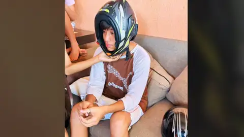 Joven que se puso del revés el casco de la moto Foto frontal del joven sentado con el casco del revés