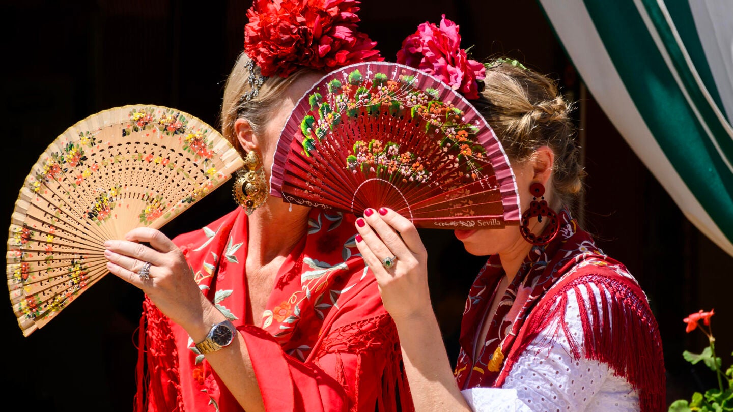 Dos mujeres vestidas de flamenca evitan mirar a los borrachos en el Real de la Feria de Abril de Sevilla