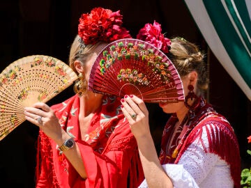 Dos mujeres vestidas de flamenca evitan mirar a los borrachos en el Real de la Feria de Abril de Sevilla