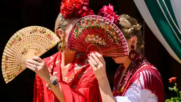Dos mujeres vestidas de flamenca evitan mirar a los borrachos en el Real de la Feria de Abril de Sevilla