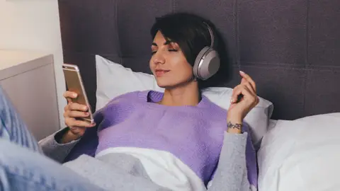 Mujer escuchando un podcast en la cama Mujer escuchando un podcast en la cama