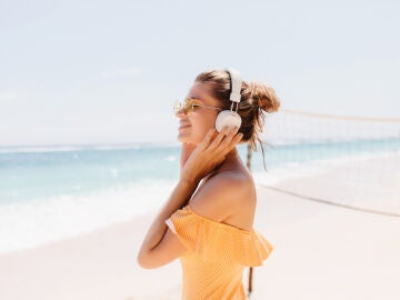 Imagen de una mujer escuchando m&uacute;sica en la playa